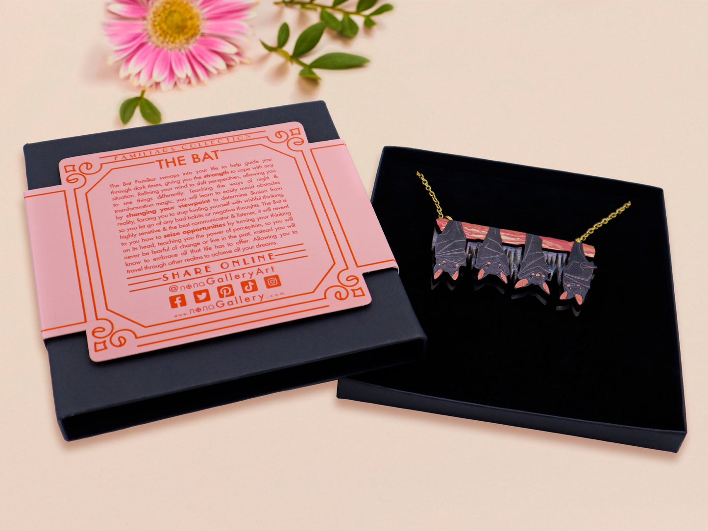 A wooden and glitter acrylic necklace with gold chain in a black box of four cute bats hung upside down on a cave wall of stalactites