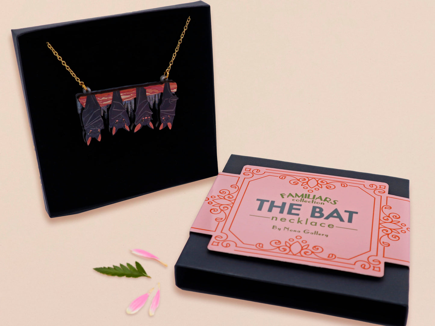 A wooden and glitter acrylic necklace with gold chain in a black box of four cute bats hung upside down on a cave wall of stalactites
