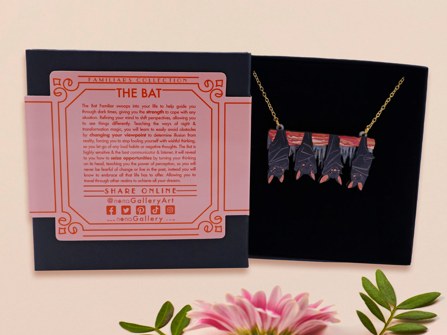 A wooden and glitter acrylic necklace with gold chain in a black box of four cute bats hung upside down on a cave wall of stalactites