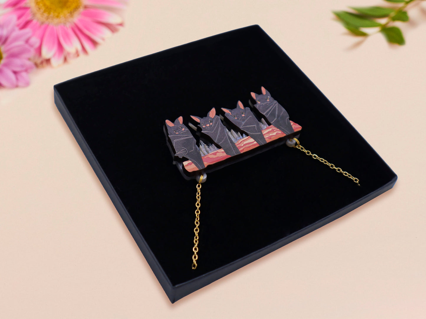 A wooden and glitter acrylic necklace with gold chain in a black box of four cute bats hung upside down on a cave wall of stalactites