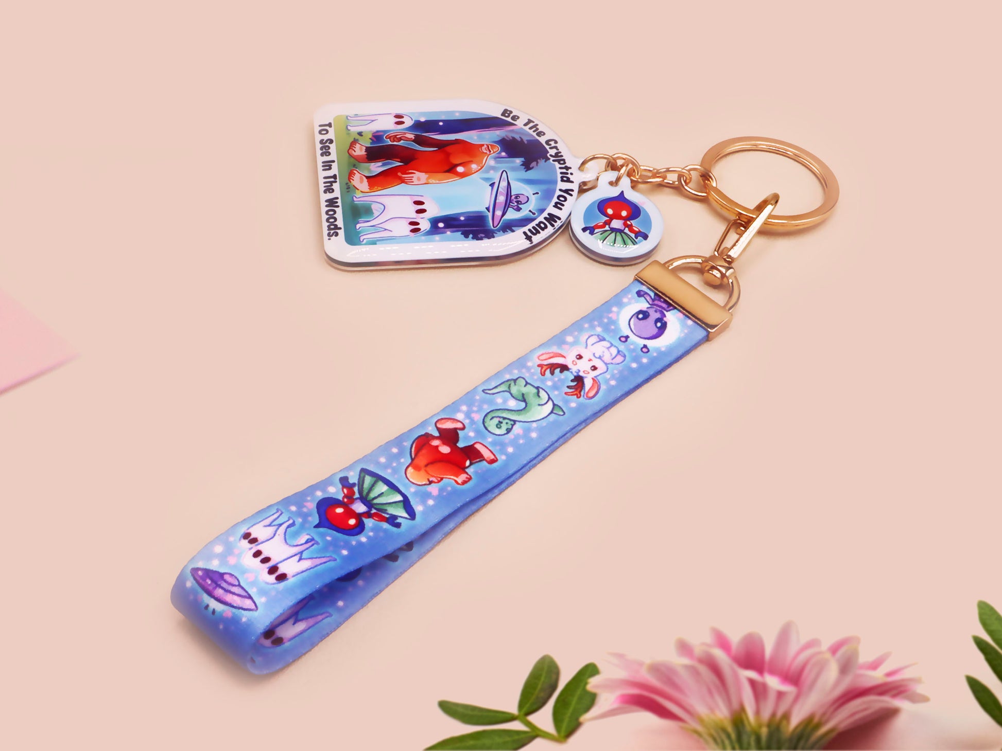 Acrylic epoxy cryptid and alien keychain with a large acrylic charm of a bigfoot yeti nightcrawlers and an alien in a UFO with the quote Be The Cryptidy You Want To See In the Woods, a smaller charm of the flatwood monster and a matching lanyard.