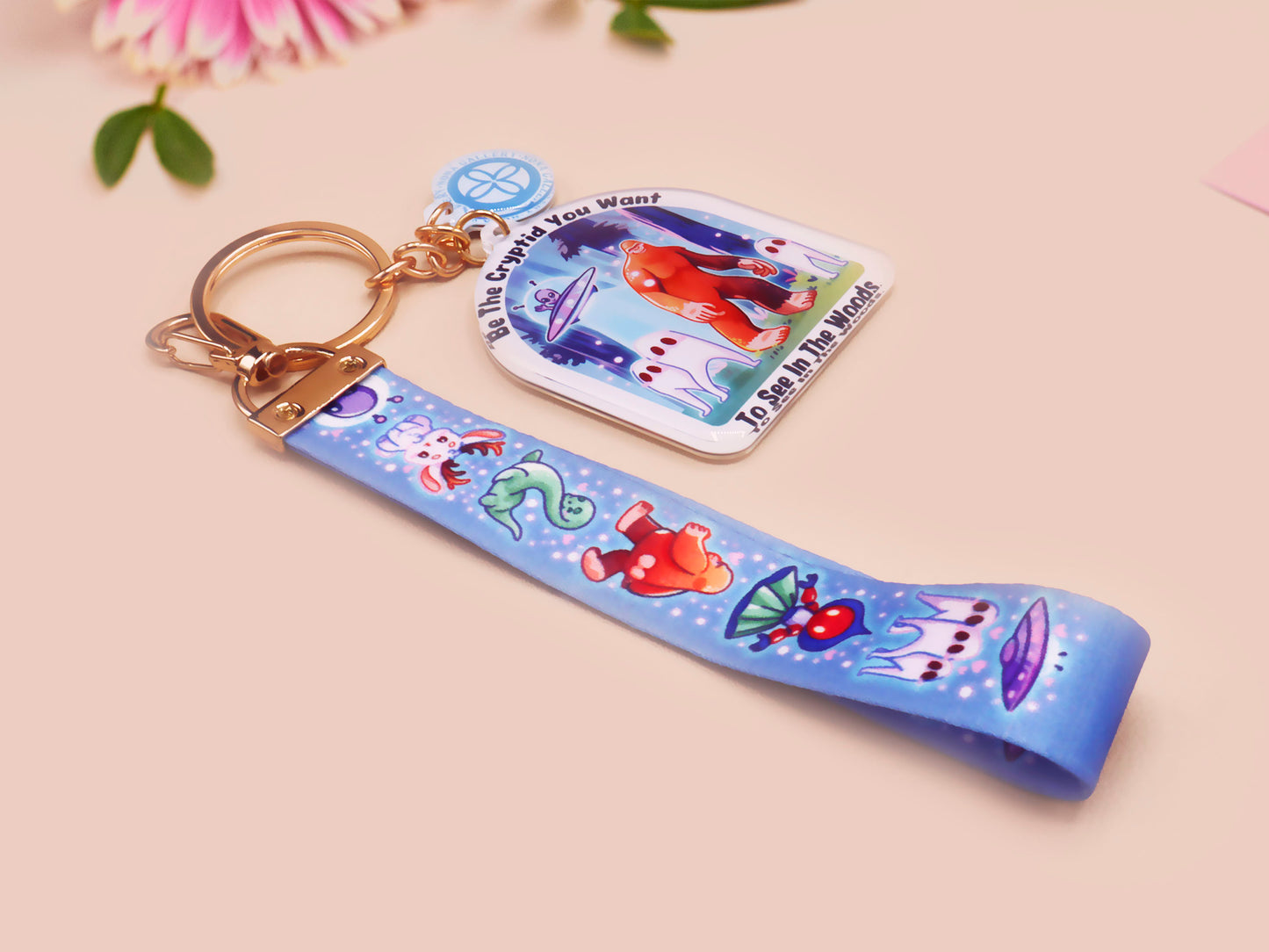 Acrylic epoxy cryptid and alien keychain with a large acrylic charm of a bigfoot yeti nightcrawlers and an alien in a UFO with the quote Be The Cryptidy You Want To See In the Woods, a smaller charm of the flatwood monster and a matching lanyard.
