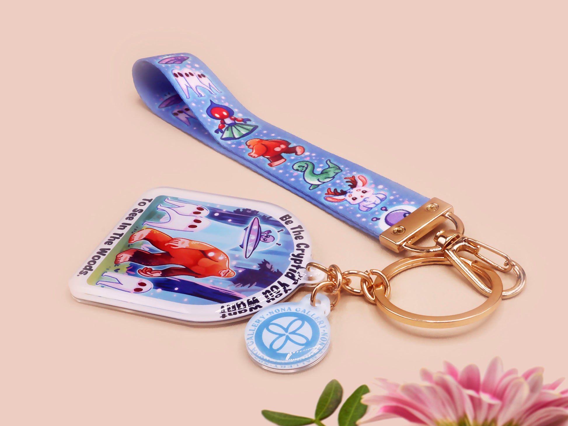 Acrylic epoxy cryptid and alien keychain with a large acrylic charm of a bigfoot yeti nightcrawlers and an alien in a UFO with the quote Be The Cryptidy You Want To See In the Woods, a smaller charm of the flatwood monster and a matching lanyard.