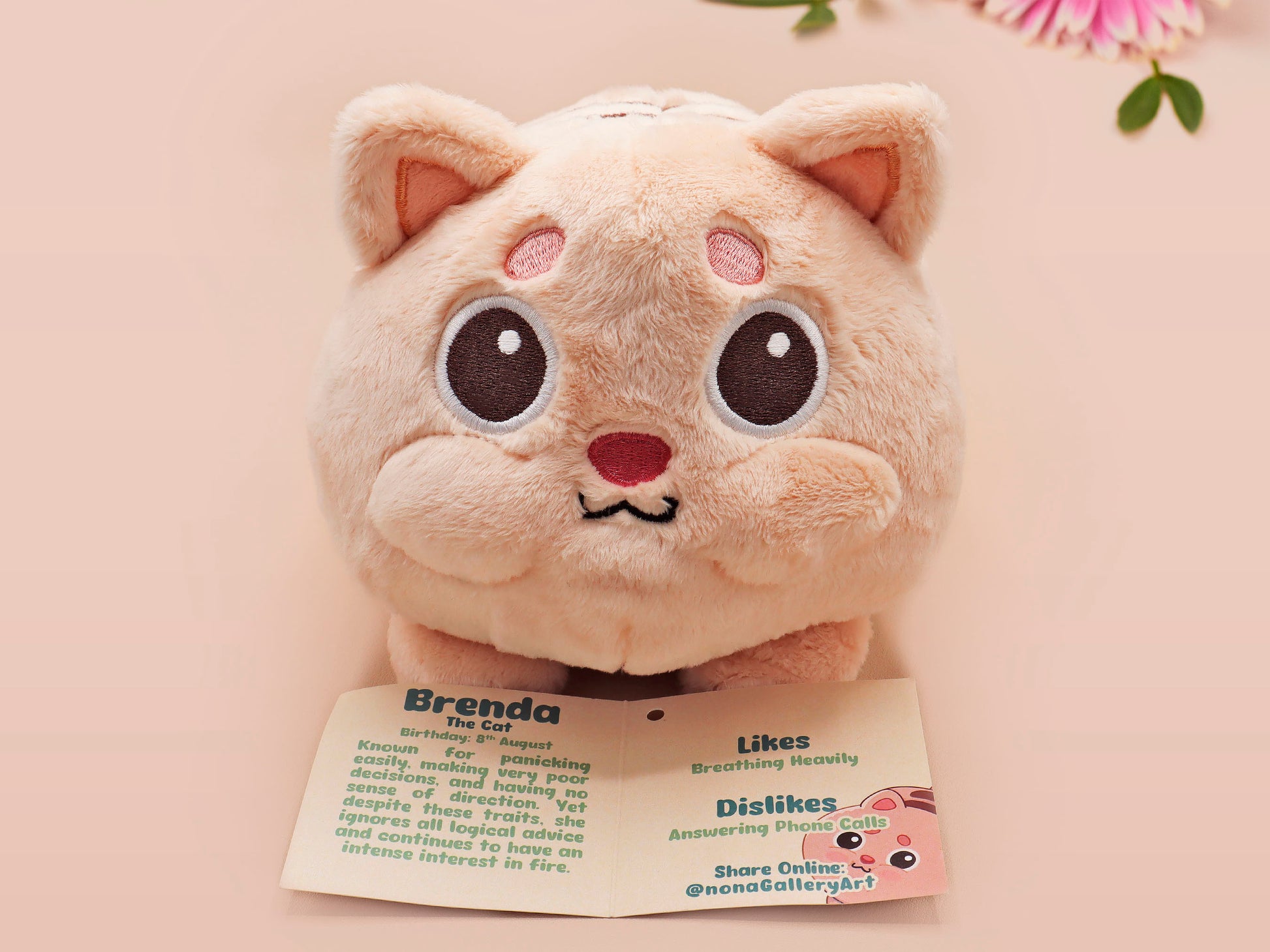 An adorable fluffy cat plushie toy with cute embroidered eyes, facial expression and applique stripes and pawprint toe beans, with a hang tag describing the cat as Brenda.