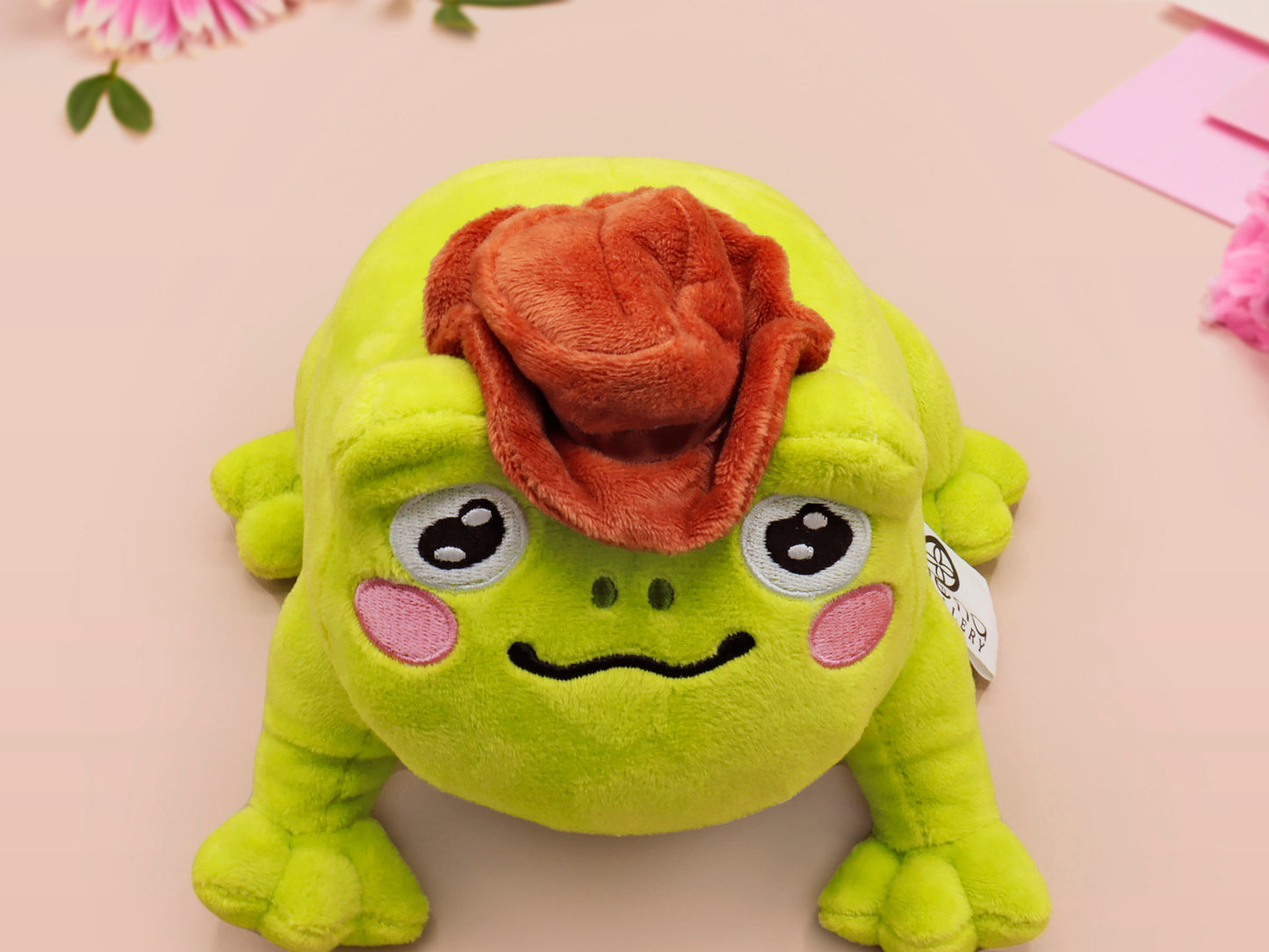 An adorable green frog plushie toy with cute embroidered eyes and facial expression, wearing a cowboy hat with a brown ribbon, and a hang tag describing the frog as Carl.