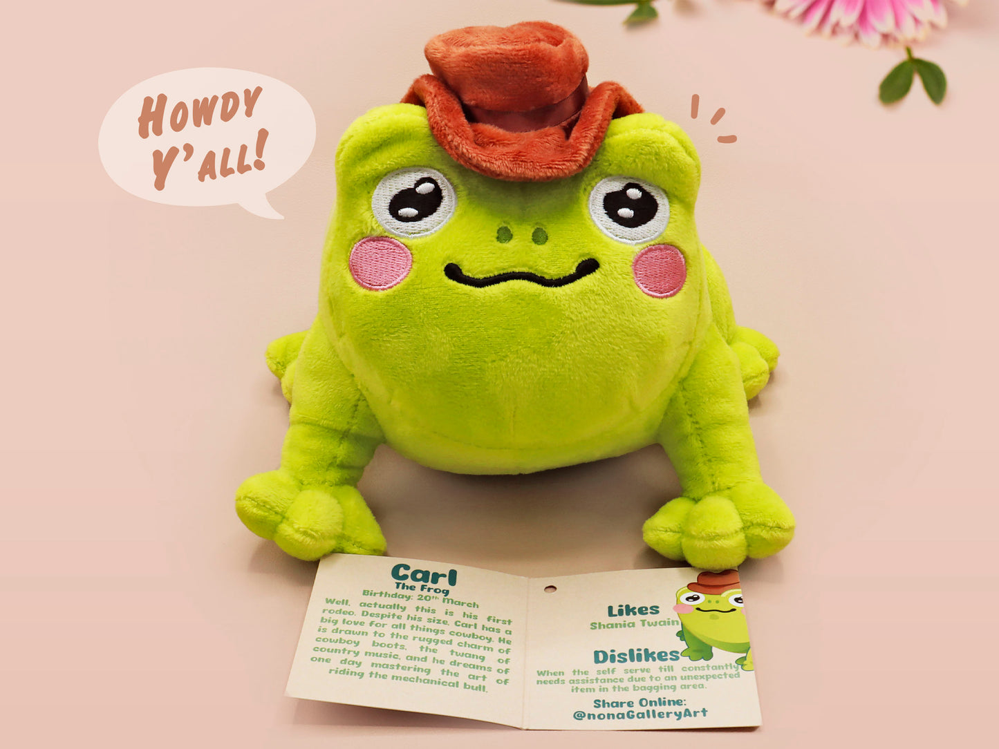 An adorable green frog plushie toy with cute embroidered eyes and facial expression, wearing a cowboy hat with a brown ribbon, and a hang tag describing the frog as Carl.