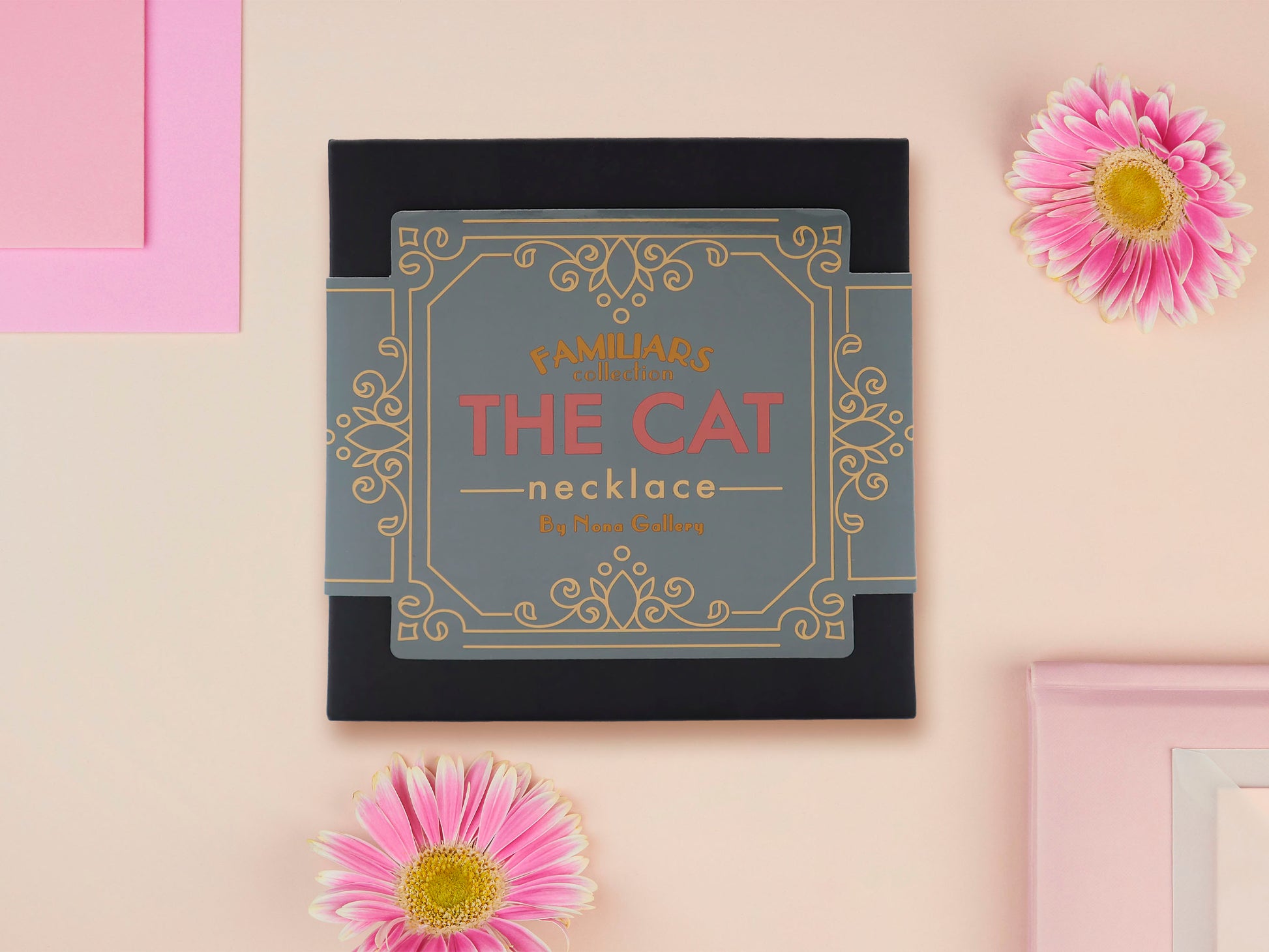 A wooden and glitter acrylic necklace with gold chain in a black box of a cute fat ginger cat sat on a shelf mischievously pushing a cactus of the end of the shelf, whilst sat next to a crystal ball and potions