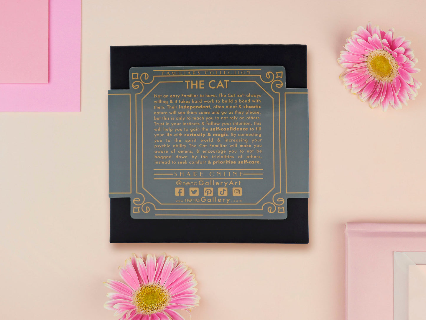A wooden and glitter acrylic necklace with gold chain in a black box of a cute fat ginger cat sat on a shelf mischievously pushing a cactus of the end of the shelf, whilst sat next to a crystal ball and potions
