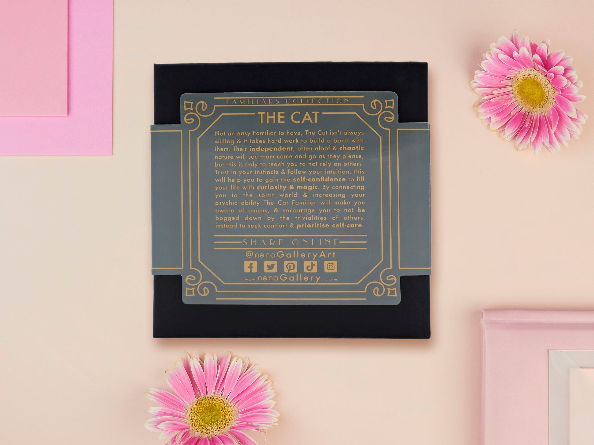 A wooden and glitter acrylic necklace with gold chain in a black box of a cute fat ginger cat sat on a shelf mischievously pushing a cactus of the end of the shelf, whilst sat next to a crystal ball and potions