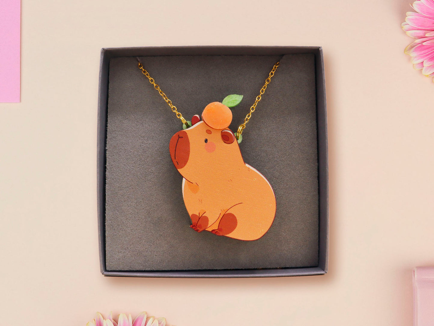 Adorable cute capybara with an orange on its head necklace made of wood and glitter pearlescent acrylic with a gold chain, displayed in a velvet gift box with a unique cute capybara sleeve design.