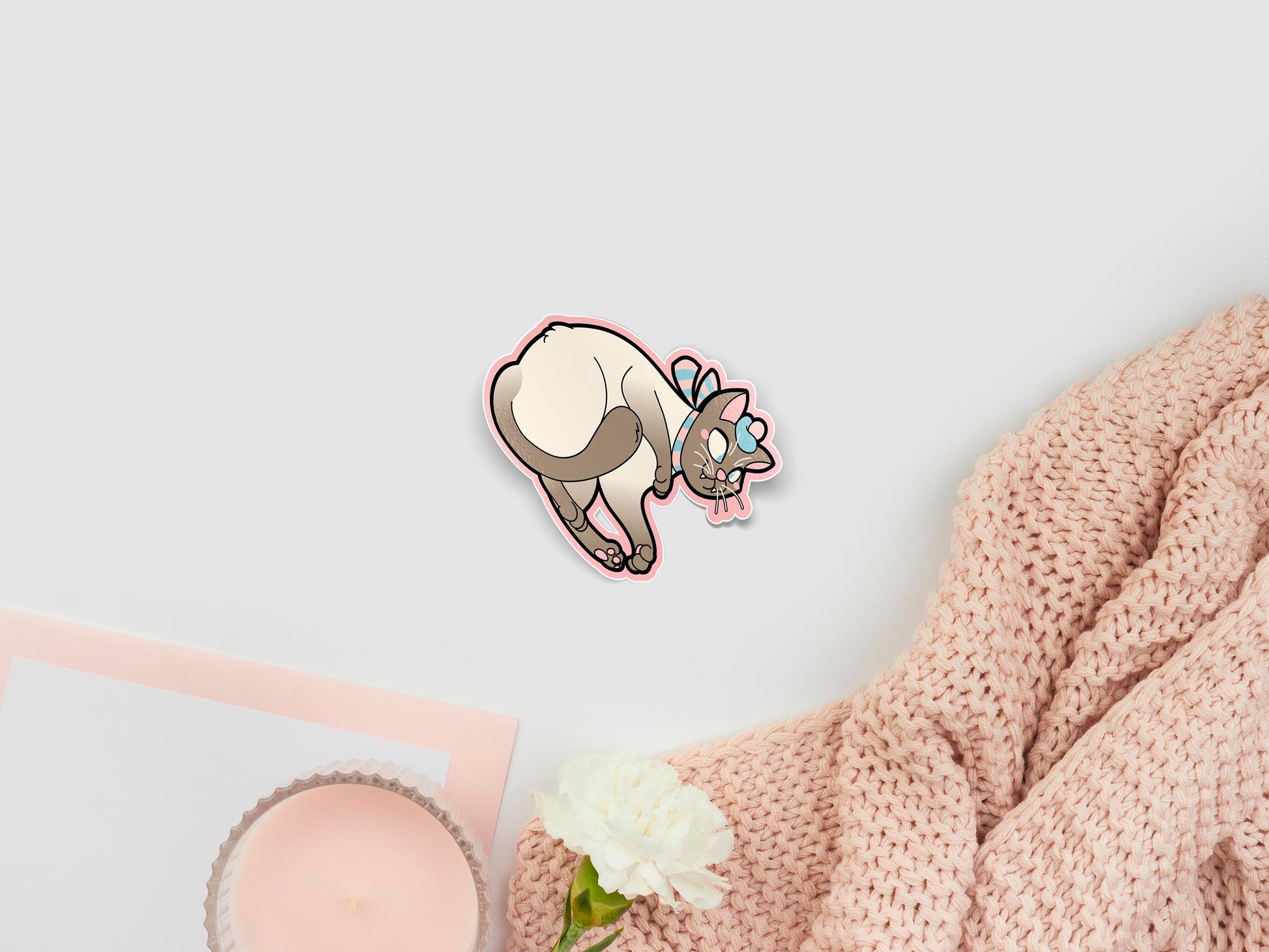 Large sticker of digital illustration cartoon of a cute Siamese cat lying on it's back wearing a blue and pink tammie bonnet and scarf