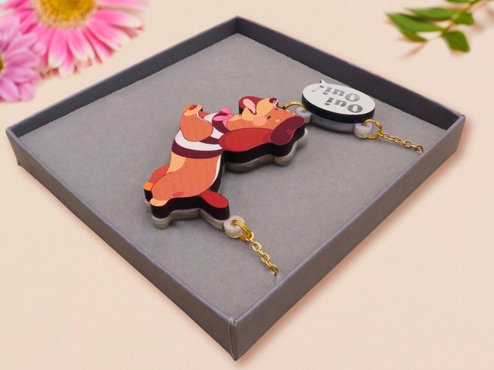 An adorable cute dachshund sausage dog necklace in a french outfit, a beret and striped top, connected to a speech bubble that is engraved with the words oui oui! displayed in a velvet gift box with a unique cute dachshund sleeve design.