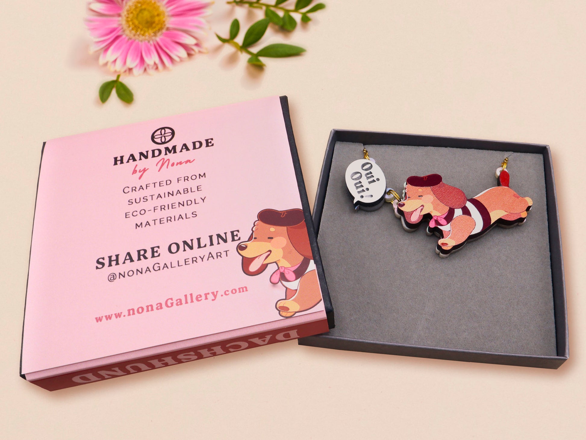 An adorable cute dachshund sausage dog necklace in a french outfit, a beret and striped top, connected to a speech bubble that is engraved with the words oui oui! displayed in a velvet gift box with a unique cute dachshund sleeve design.