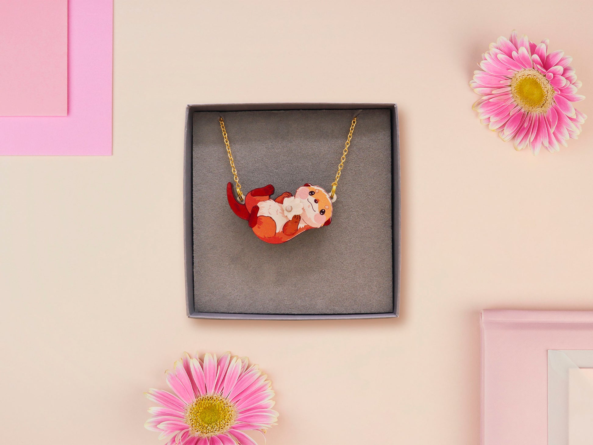 An adorable cute otter holding a clam seashell with a pearl inside necklace made of wood and glitter pearlescent acrylic with a gold chain is displayed in a velvet gift box with a unique cute otter sleeve design.
