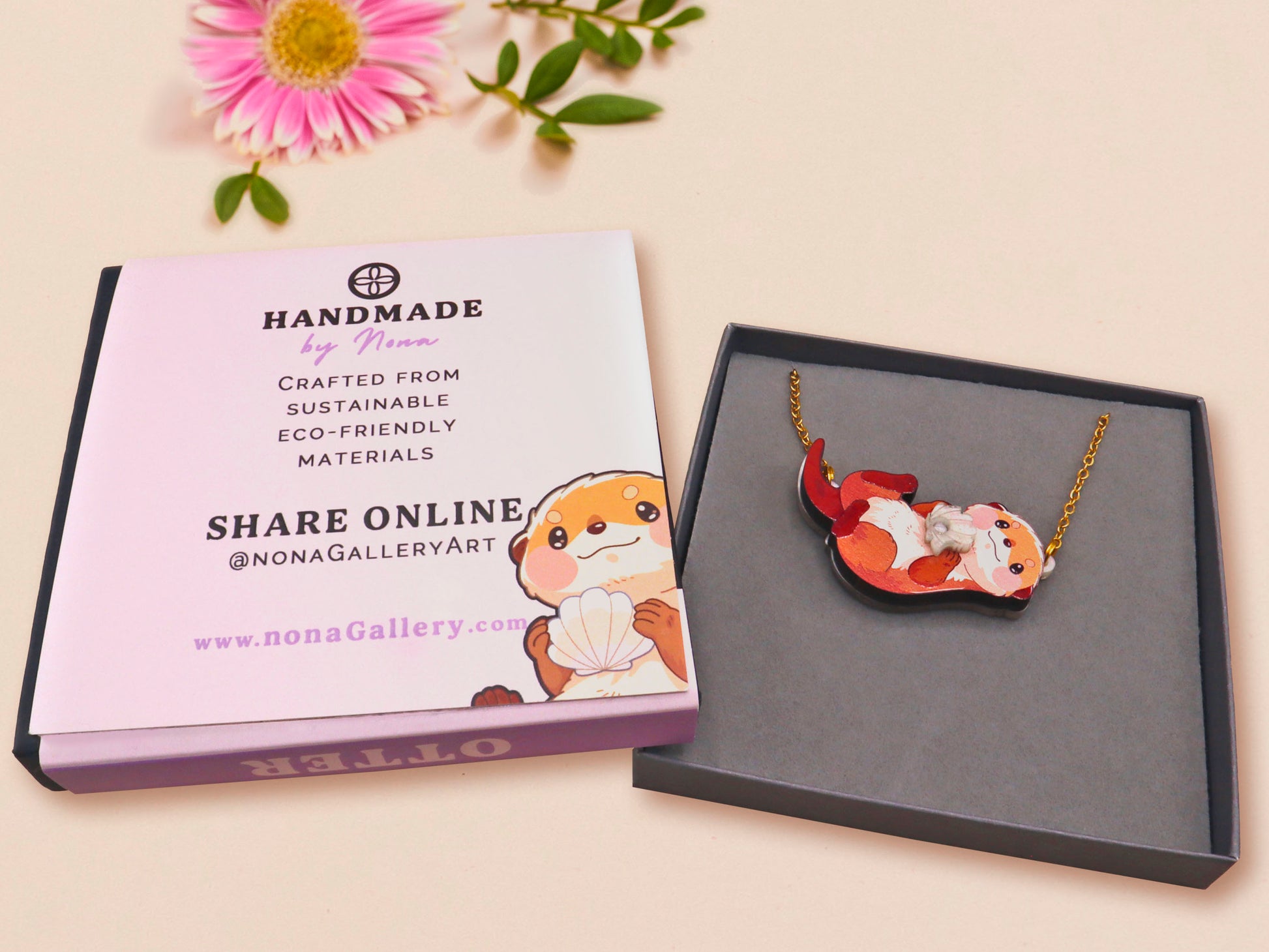 An adorable cute otter holding a clam seashell with a pearl inside necklace made of wood and glitter pearlescent acrylic with a gold chain is displayed in a velvet gift box with a unique cute otter sleeve design.