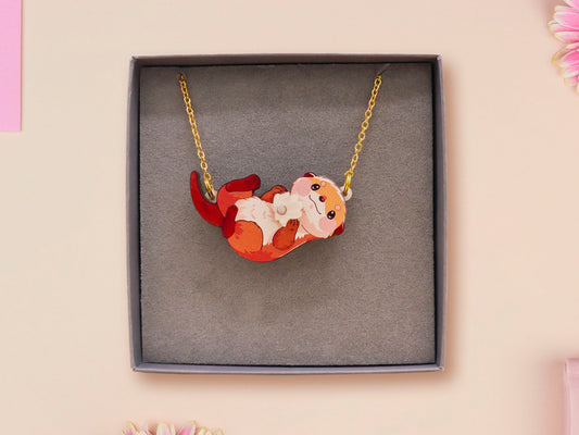 An adorable cute otter holding a clam seashell with a pearl inside necklace made of wood and glitter pearlescent acrylic with a gold chain is displayed in a velvet gift box with a unique cute otter sleeve design.