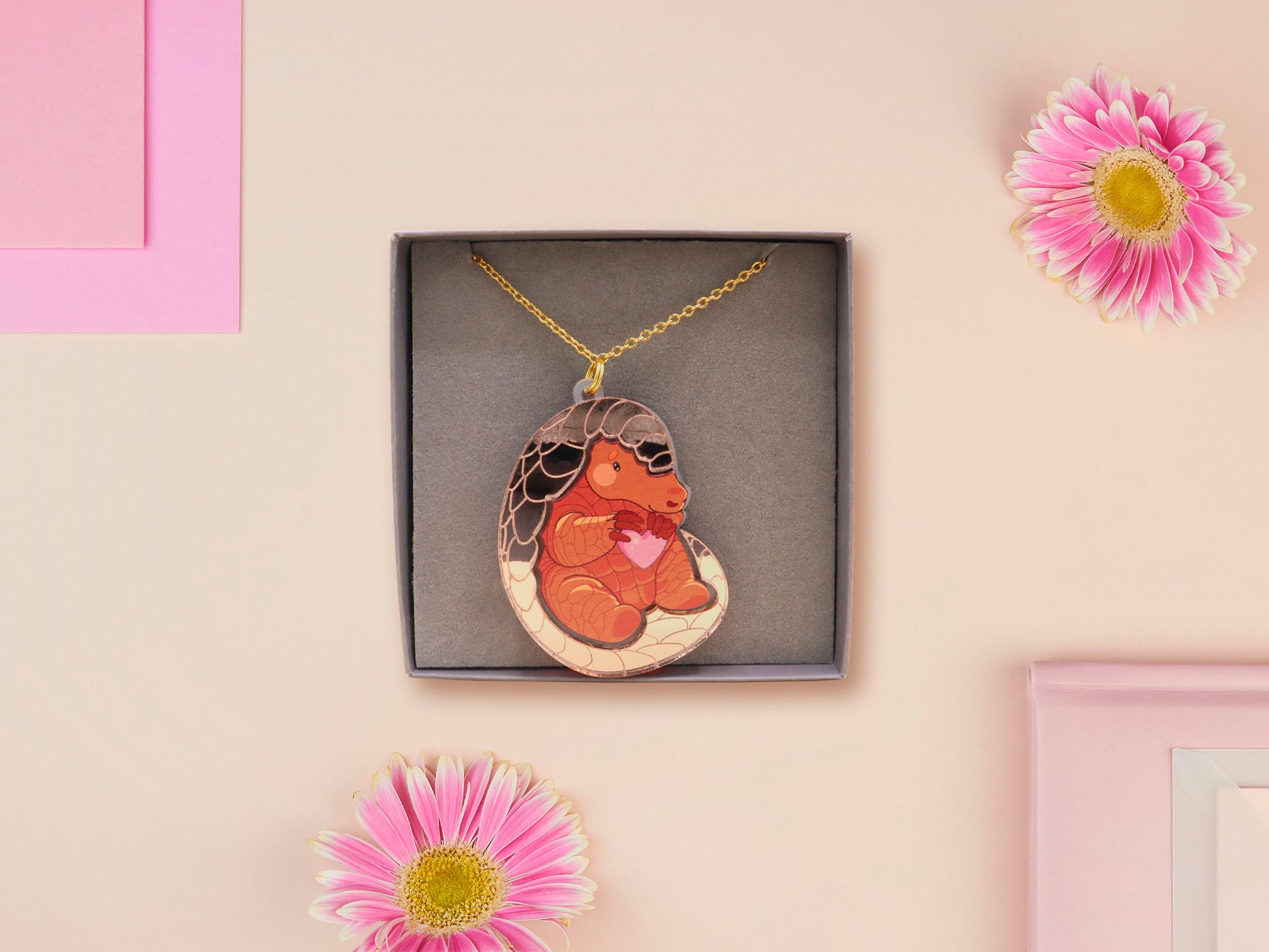 An adorable shy pangolin aardvark holding a heart necklace made of wood and glitter mirror acrylic with a gold chain is displayed in a velvet gift box with a unique cute Pangolin sleeve design.