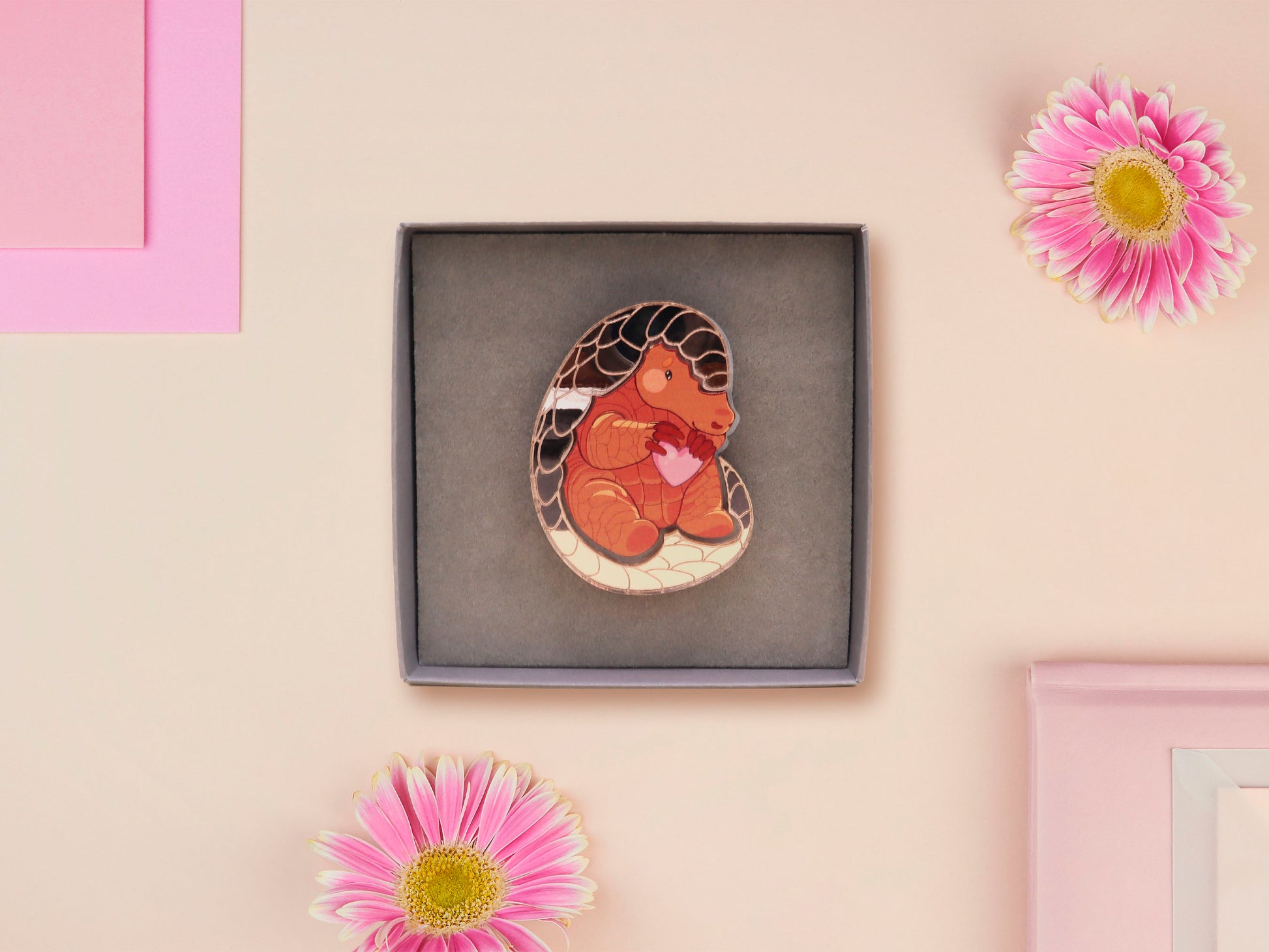 An adorable shy pangolin aardvark holding a heart brooch pin badge made of wood and glitter mirror acrylic with a gold chain is displayed in a velvet gift box with a unique cute Pangolin sleeve design.