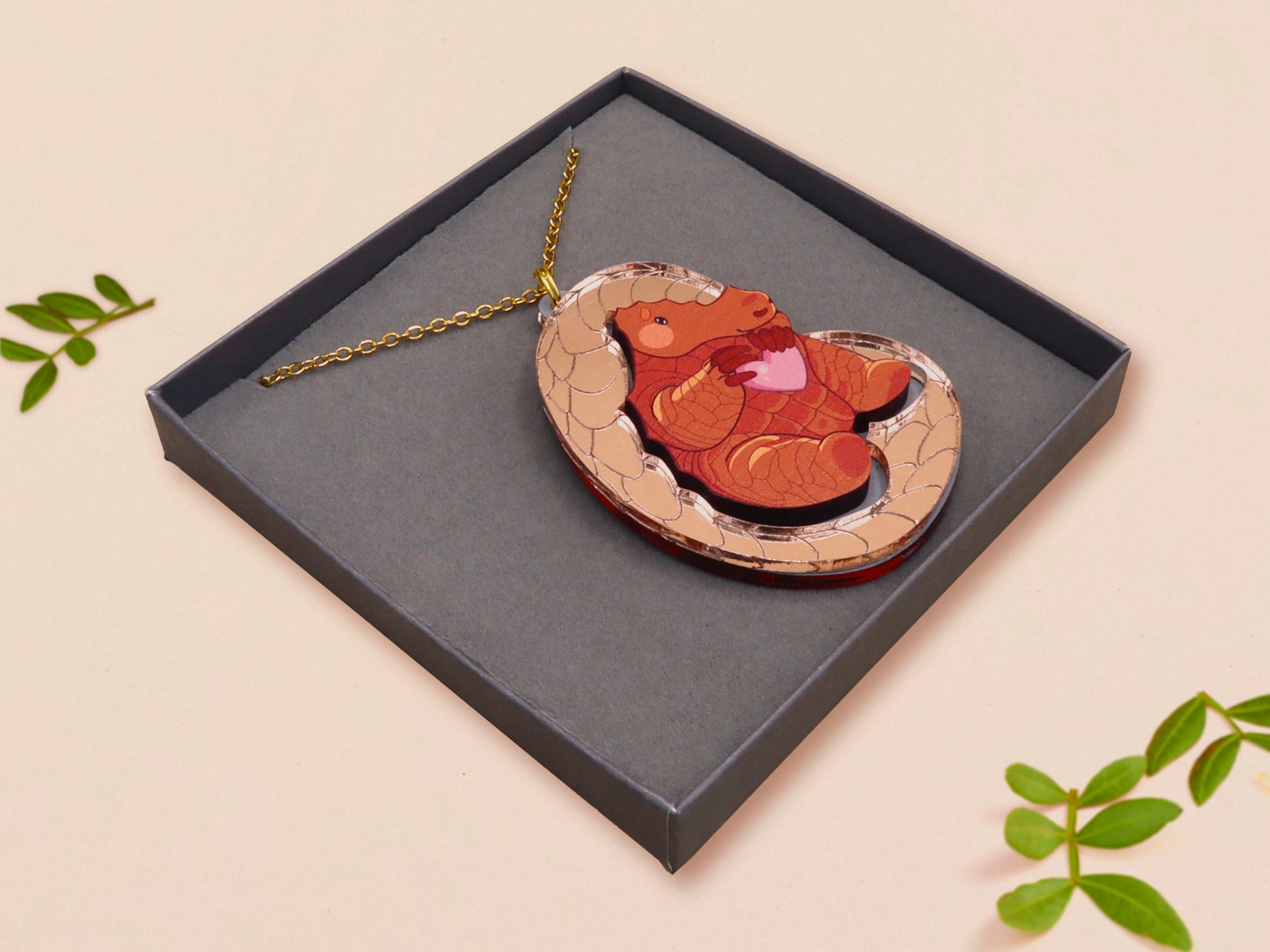 An adorable shy pangolin aardvark holding a heart necklace made of wood and glitter mirror acrylic with a gold chain is displayed in a velvet gift box with a unique cute Pangolin sleeve design.