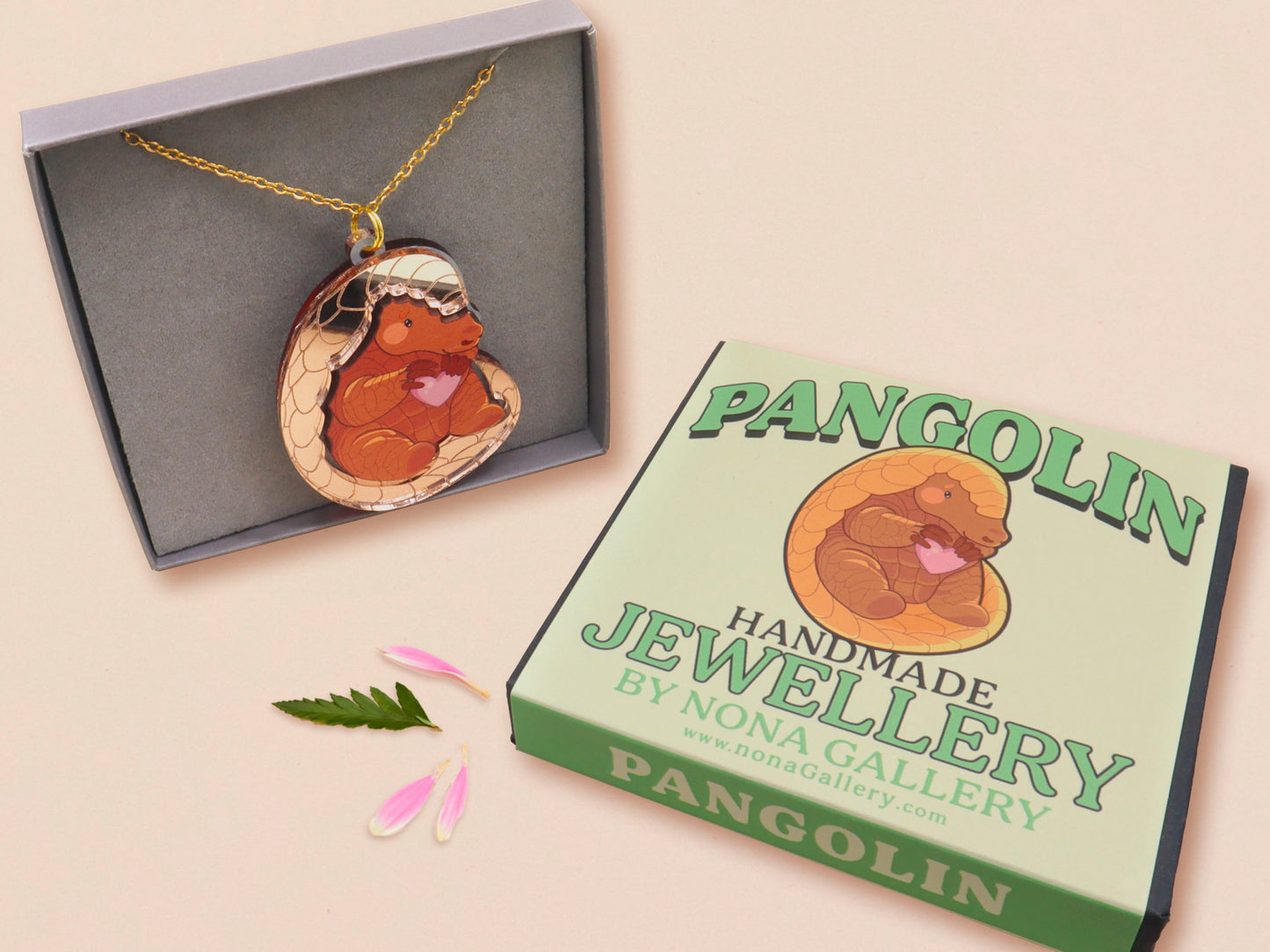 An adorable shy pangolin aardvark holding a heart necklace made of wood and glitter mirror acrylic with a gold chain is displayed in a velvet gift box with a unique cute Pangolin sleeve design.