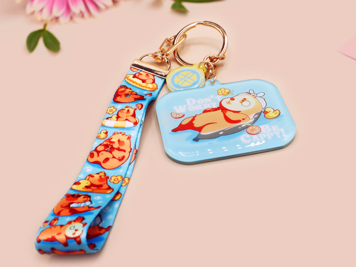 Acrylic epoxy blue capybara spa keychain with a large acrylic charm of a capybara floating in water relaxing with a face mask with the quote don't worry be cappy, a smaller charm of a cute rubber duck and a matching capybara spa day lanyard.