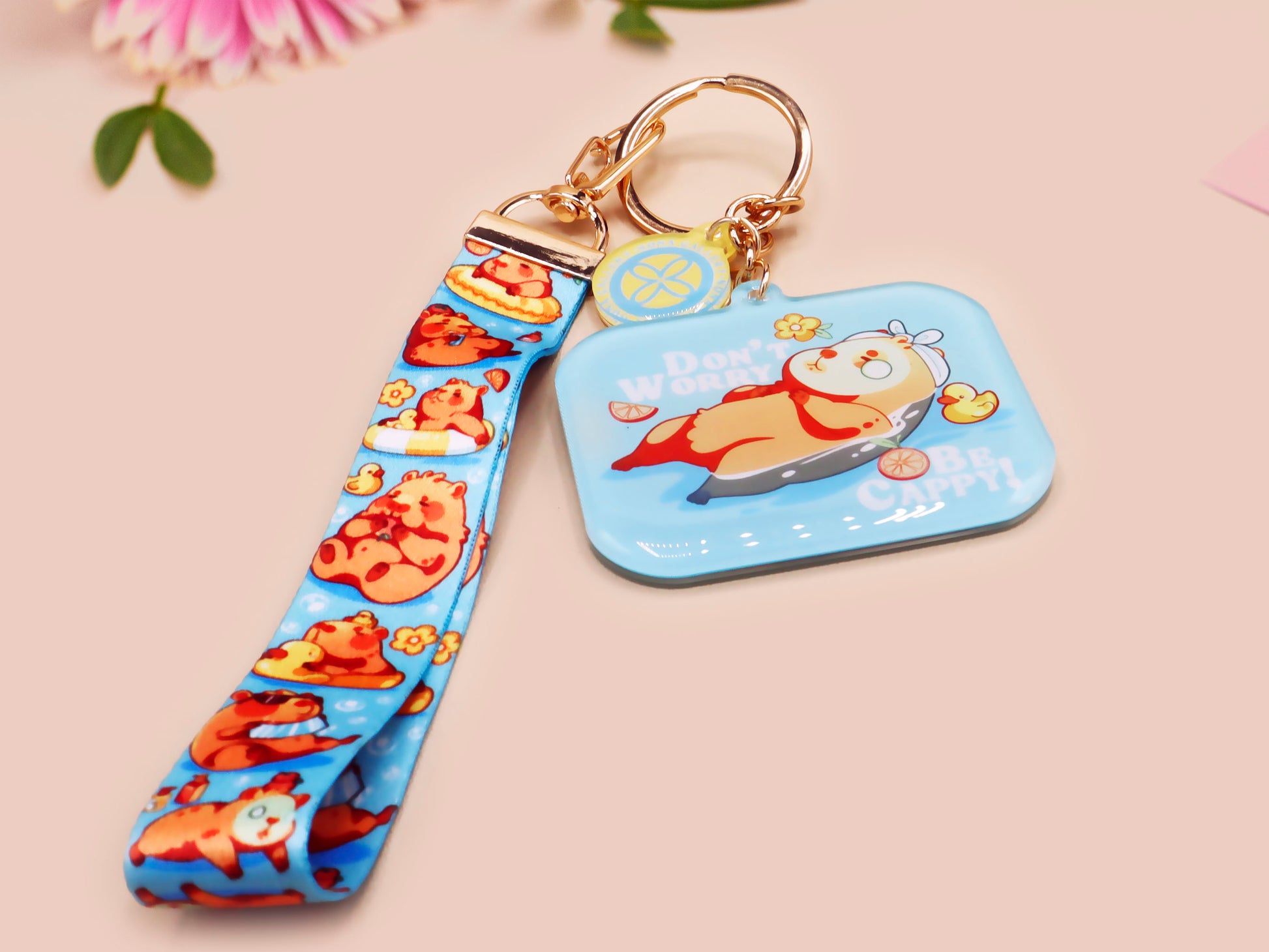 Acrylic epoxy blue capybara spa keychain with a large acrylic charm of a capybara floating in water relaxing with a face mask with the quote don't worry be cappy, a smaller charm of a cute rubber duck and a matching capybara spa day lanyard.