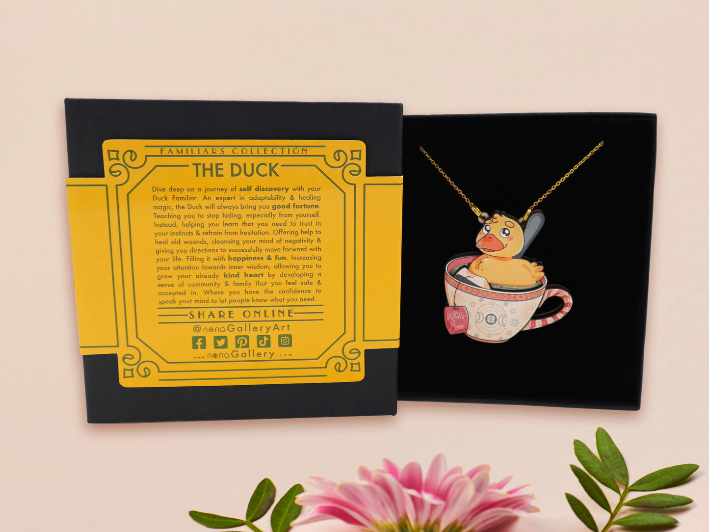Mixed material handmade necklace of chibi cartoon duck sat in a pearlescent witch's brew teacup, with a gold chain and black gift box with a yellow familiars collection gift sleeve