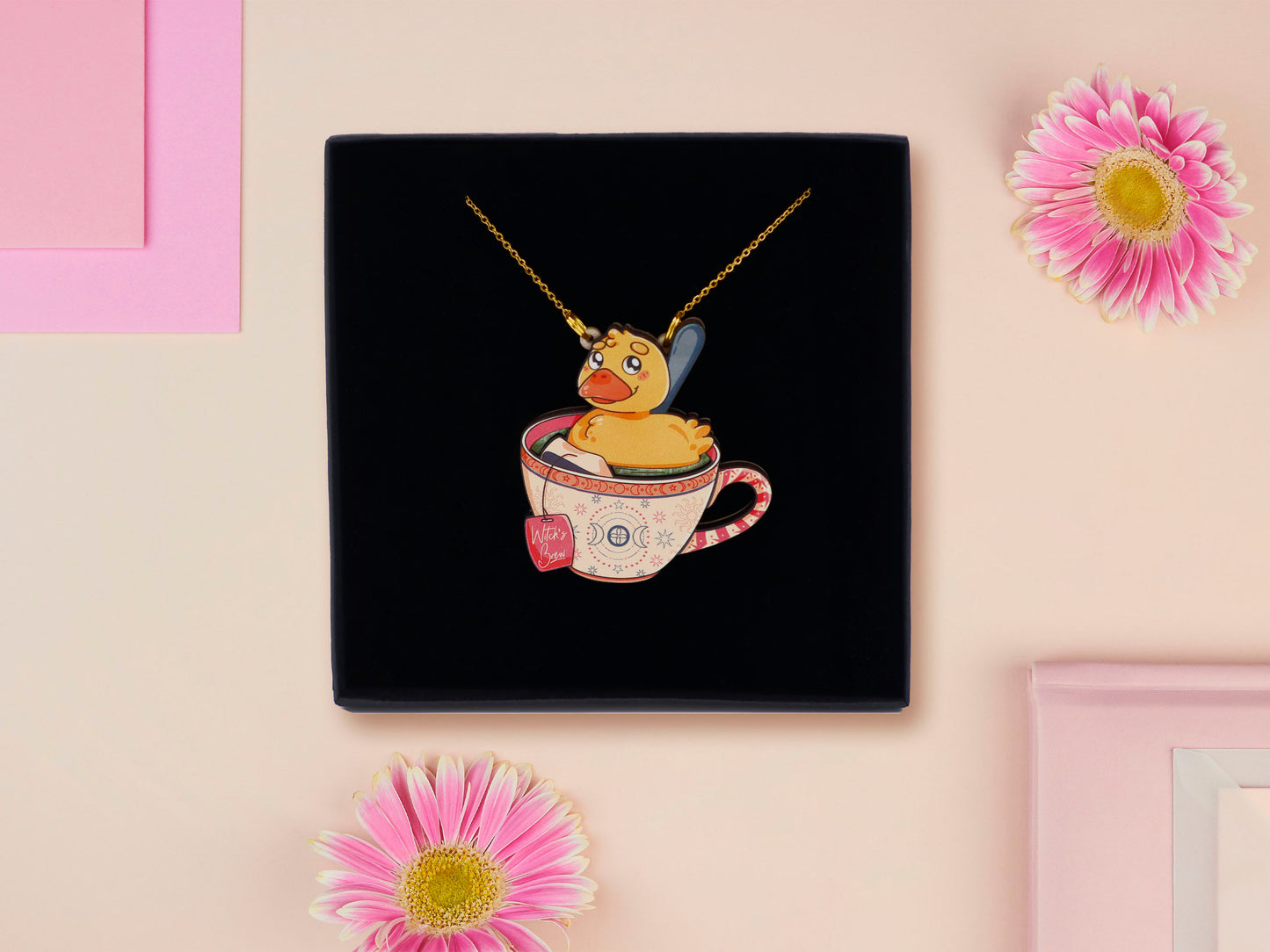 Mixed material handmade necklace of chibi cartoon duck sat in a pearlescent witch's brew teacup, with a gold chain and black gift box.
