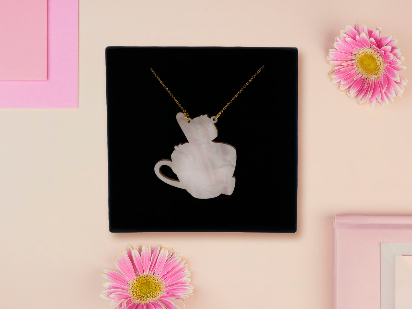 Back of mixed material handmade necklace of chibi cartoon duck sat in a pearlescent witch's brew teacup, with a gold chain and black gift box.