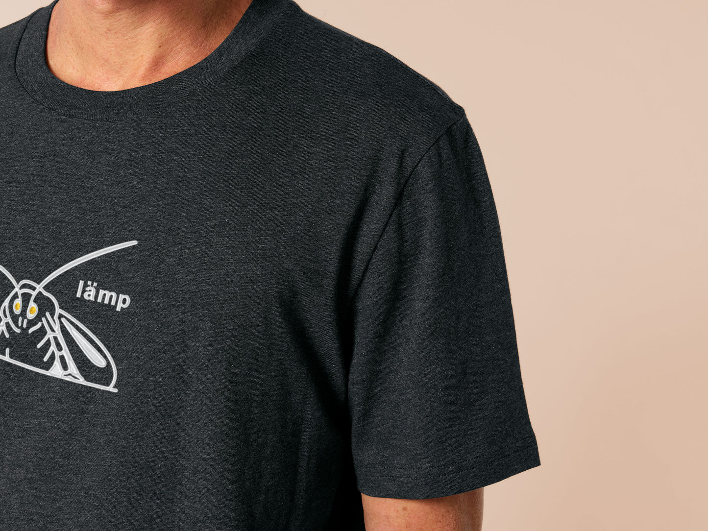 A grey crew neck short sleeve t-shirt, with an embroidered Mothman white thread design of a moth with glowing yellow eyes and the word lämp