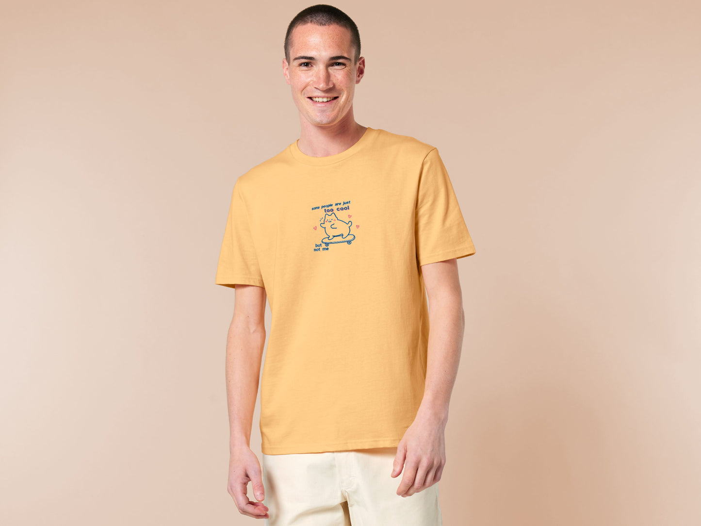 Light yellow short sleeve t-shirt with embroidered pink and blue design of a cute chibi skateboarding cat with the text some people are just too cool but not me.