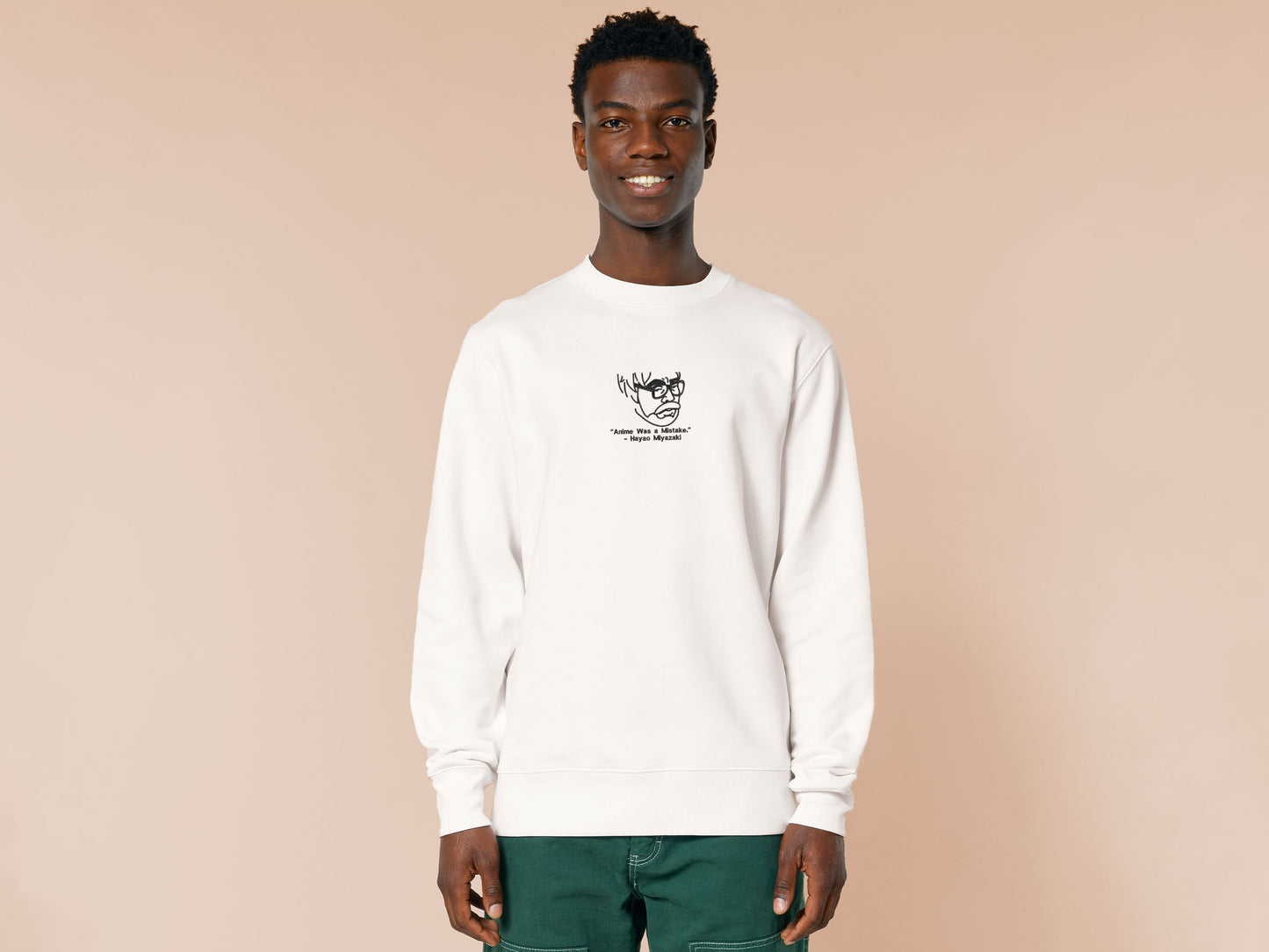 A off white crew neck long sleeve sweater, with an embroidered black thread design of a portrait of a depressed Hayao Miyazaki the creator of Studio Ghibli with text underneath that reads "Anime Was A Mistake." - Hayao Miyazaki