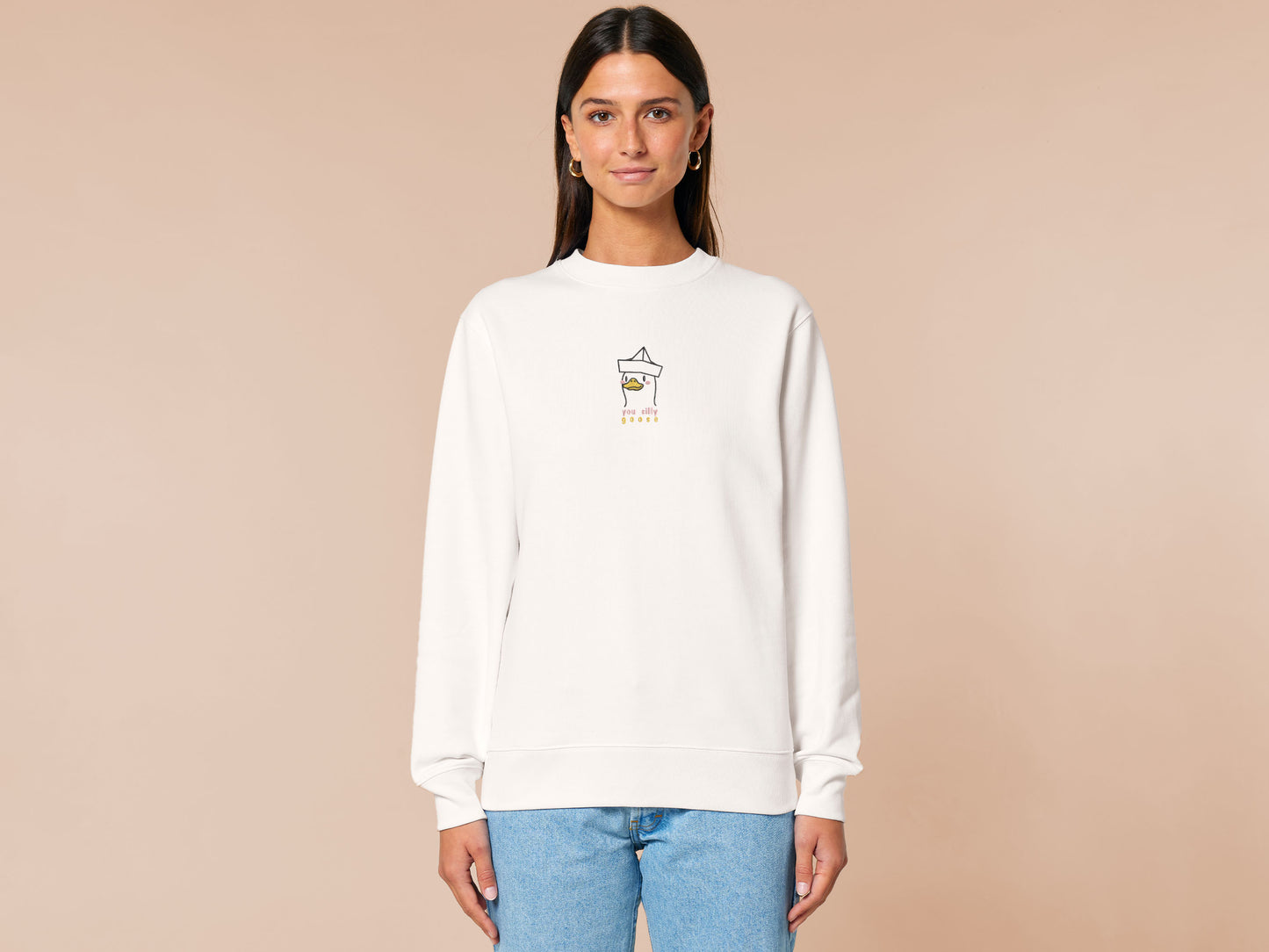 An embroidered white sweater design of a cute cartoon goose wearing a paper hat with text underneath that reads you silly goose.