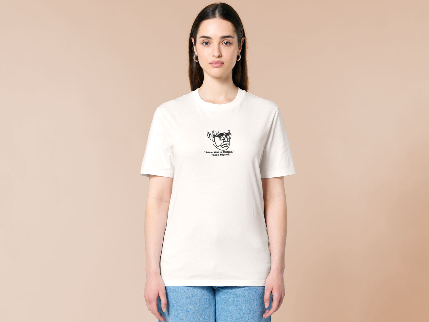 A off white crew neck short sleeve t-shirt, with an embroidered black thread design of a portrait of a depressed Hayao Miyazaki the creator of Studio Ghibli with text underneath that reads "Anime Was A Mistake." - Hayao Miyazaki