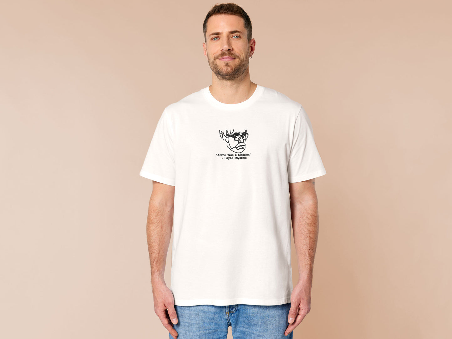 A off white crew neck short sleeve t-shirt, with an embroidered black thread design of a portrait of a depressed Hayao Miyazaki the creator of Studio Ghibli with text underneath that reads "Anime Was A Mistake." - Hayao Miyazaki