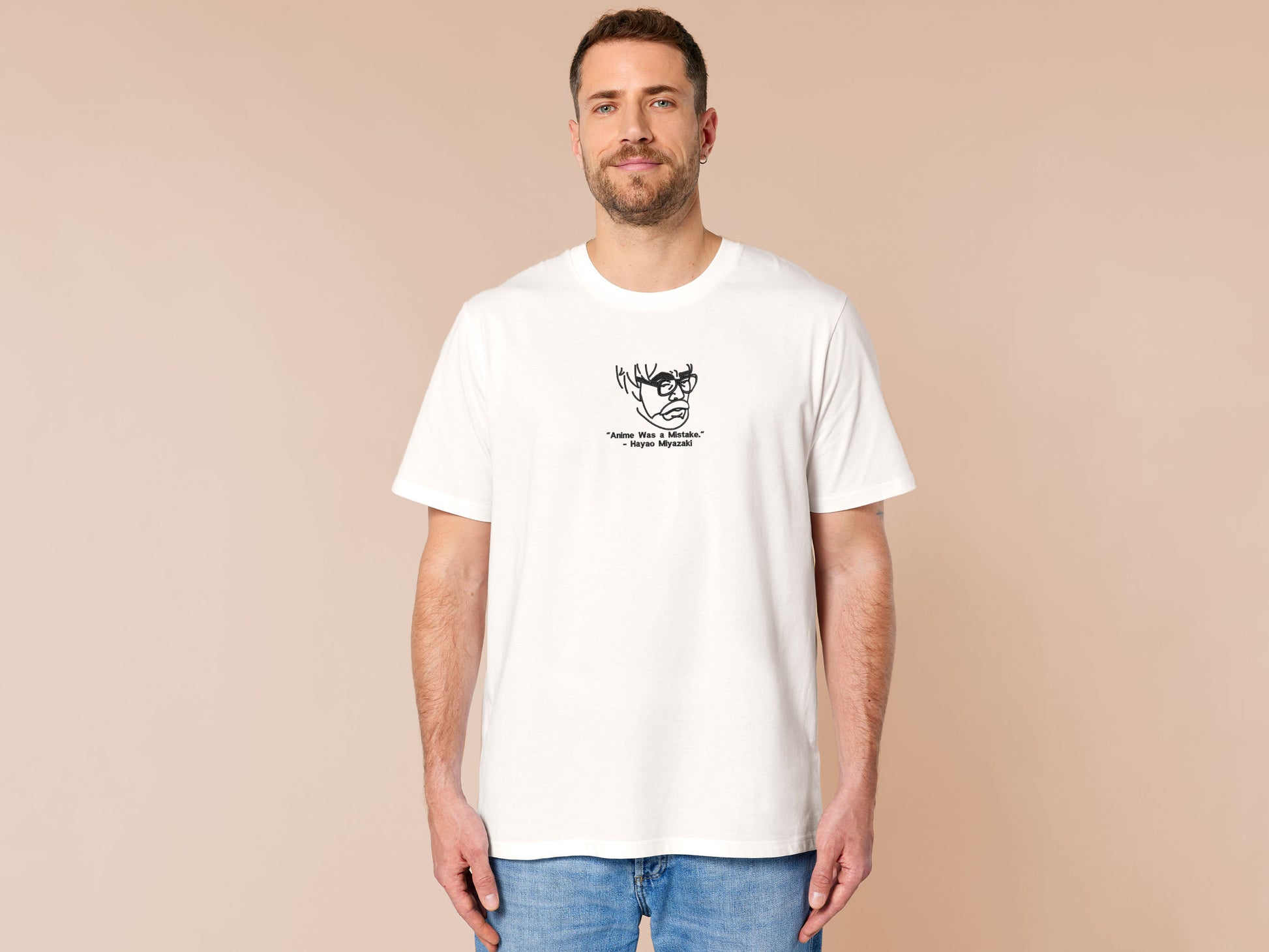 A off white crew neck short sleeve t-shirt, with an embroidered black thread design of a portrait of a depressed Hayao Miyazaki the creator of Studio Ghibli with text underneath that reads "Anime Was A Mistake." - Hayao Miyazaki