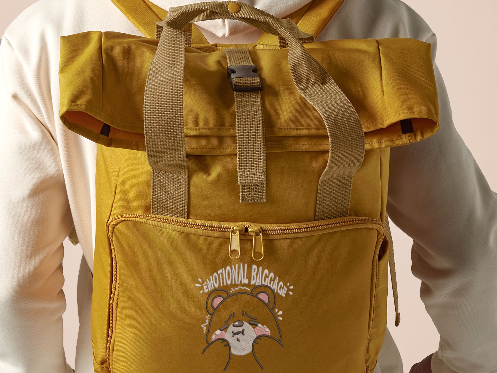 Yellow roll top twin handle backpack with an embroided design of cute crying bear and the quote emotional baggage