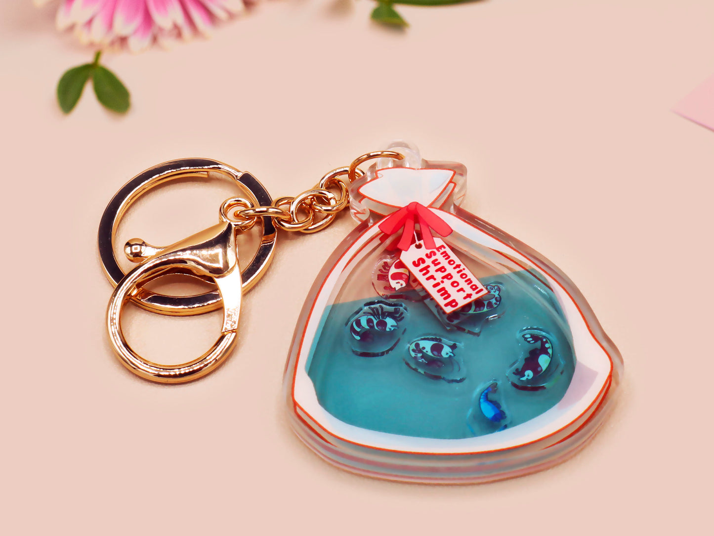 A large transparent acrylic shaker keychain with gold keyring, filled with mini chibi shrimps and labelled as emotional support shrimp