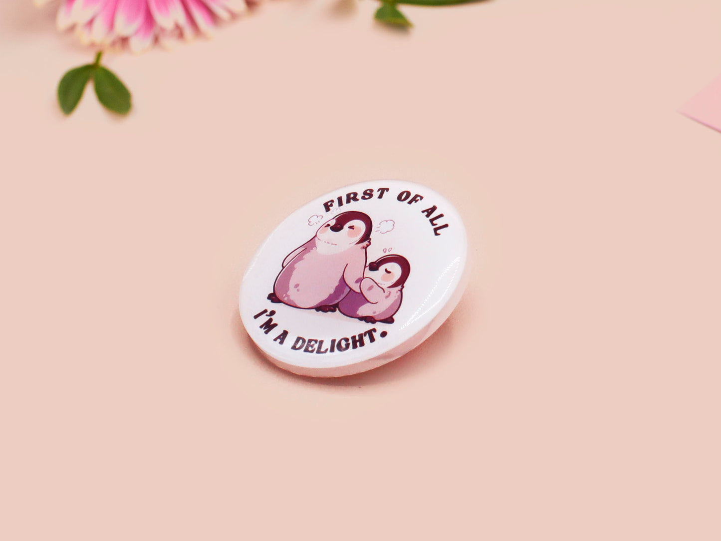 A clear acrylic pin badge with a pink heart-shaped pin back clasp. The design of the pin badge is of a cute baby penguin chicks squabbling with the quote first of all I'm a delight.