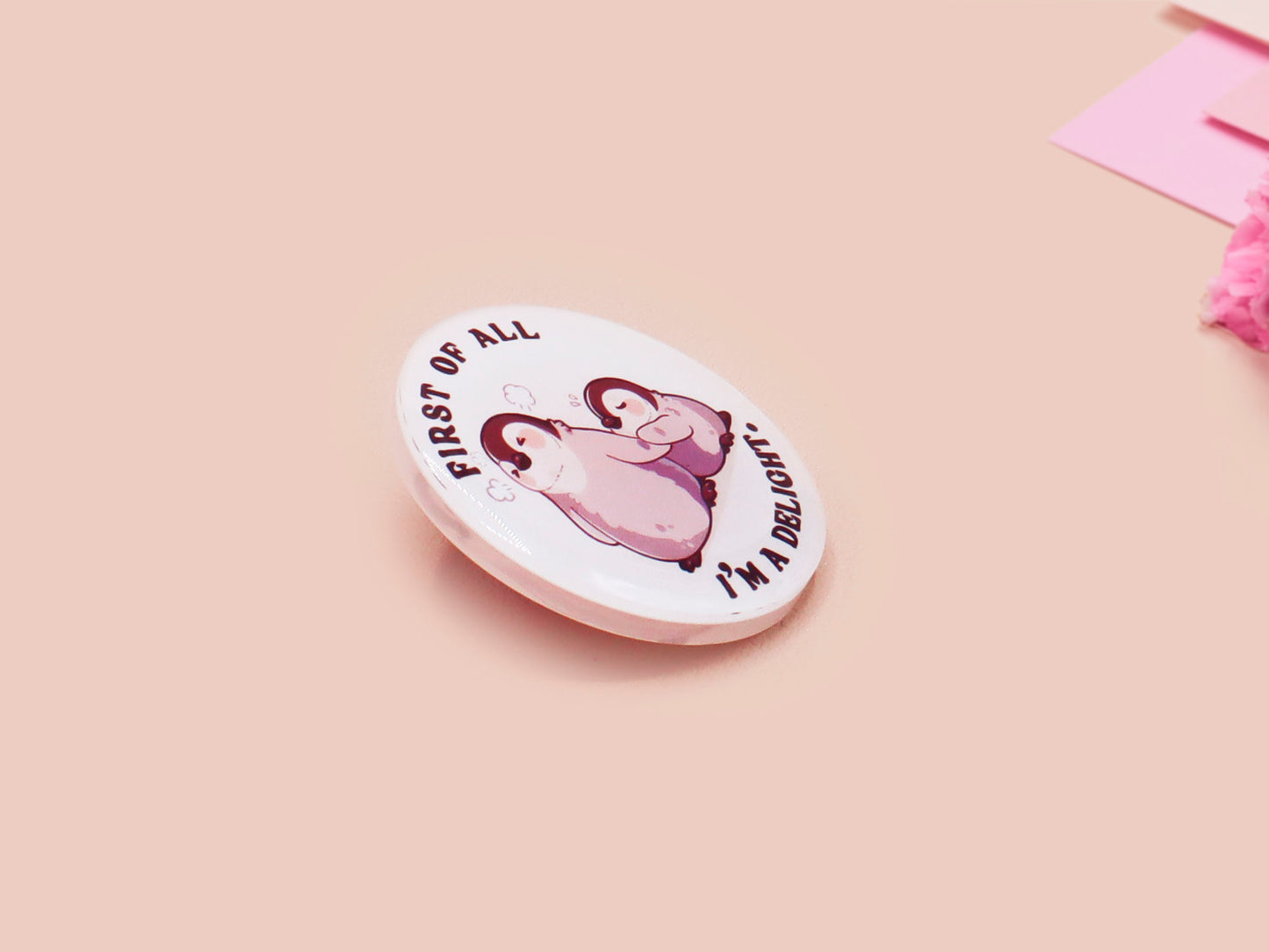 A clear acrylic pin badge with a pink heart-shaped pin back clasp. The design of the pin badge is of a cute baby penguin chicks squabbling with the quote first of all I'm a delight.
