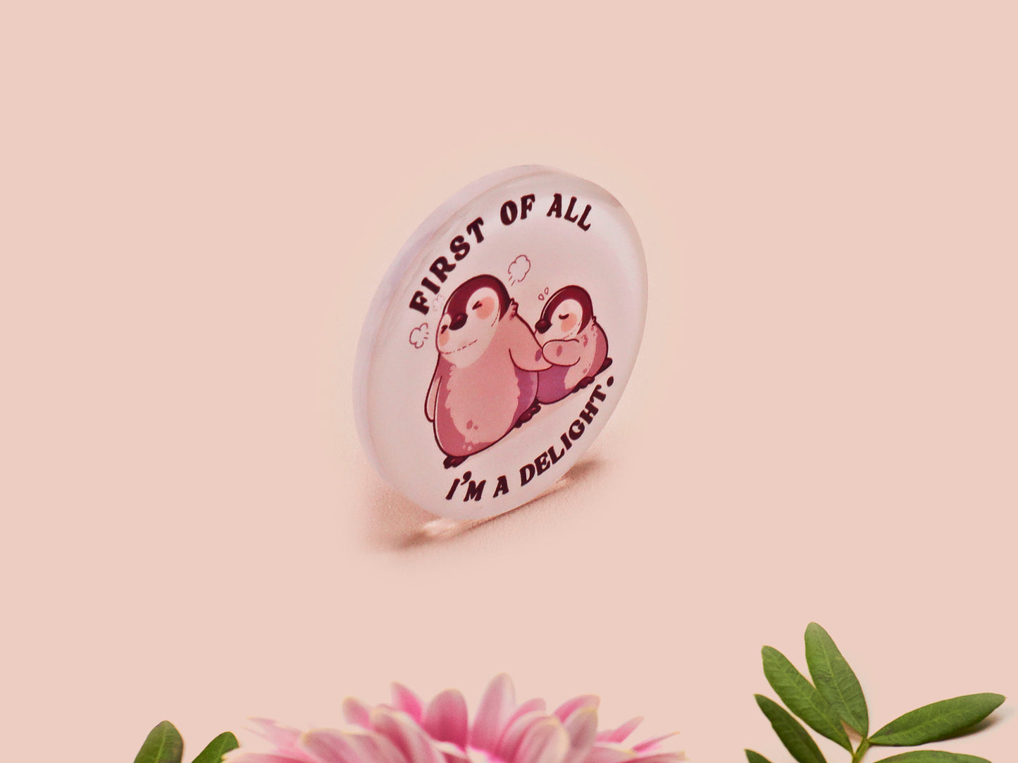 A clear acrylic pin badge with a pink heart-shaped pin back clasp. The design of the pin badge is of a cute baby penguin chicks squabbling with the quote first of all I'm a delight.
