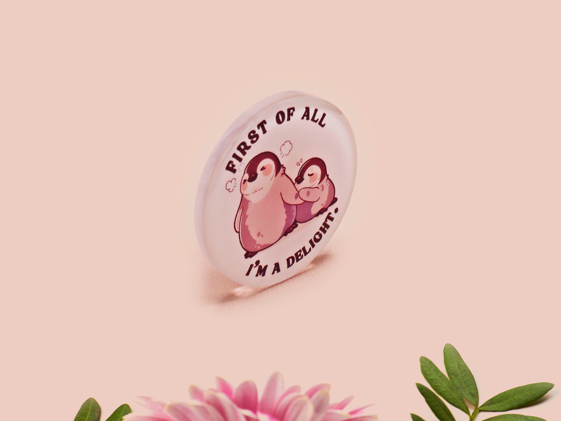 A clear acrylic pin badge with a pink heart-shaped pin back clasp. The design of the pin badge is of a cute baby penguin chicks squabbling with the quote first of all I'm a delight.