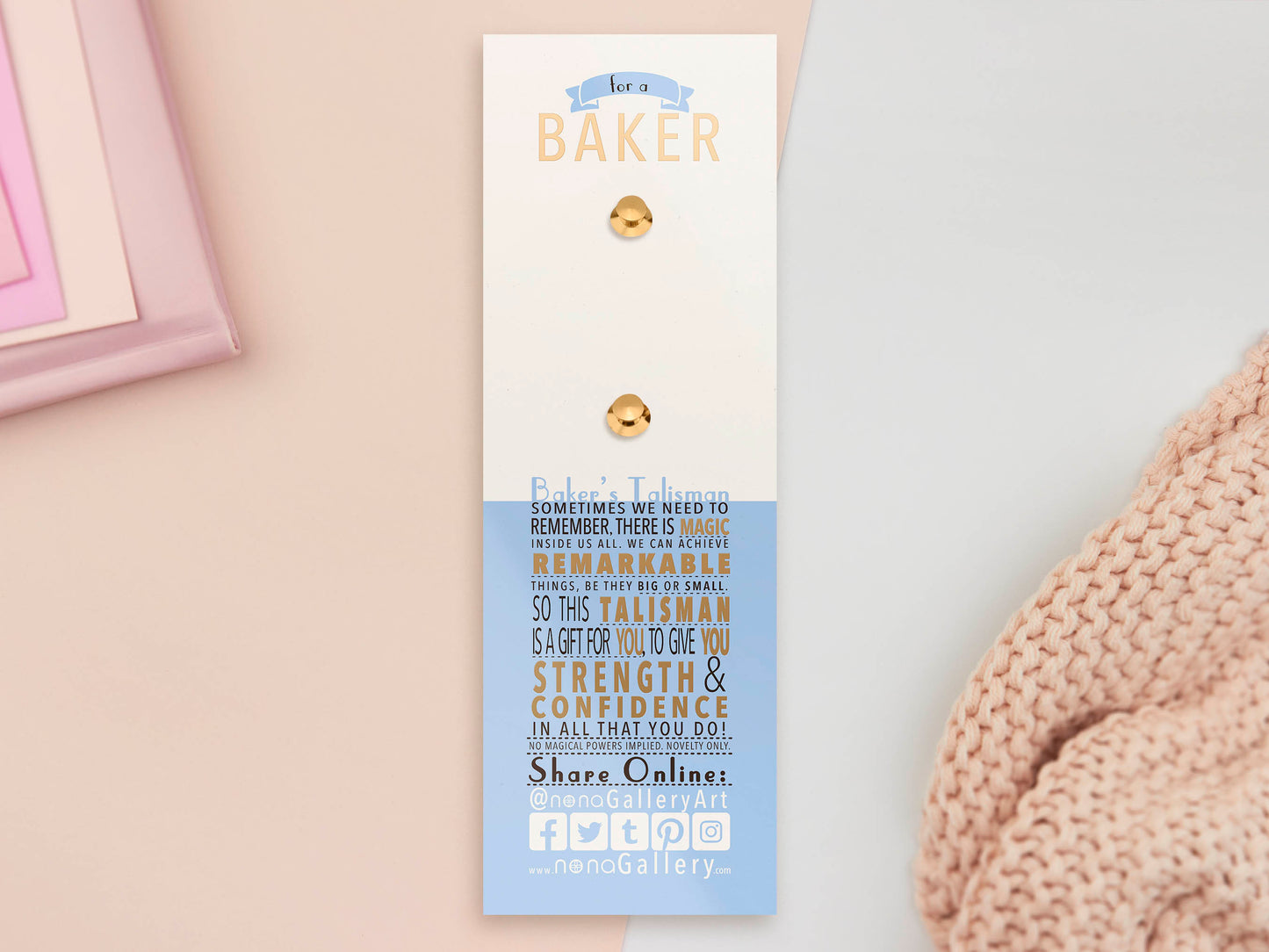 The back of the long white and blue backing card with gold accents. The backing card details the symbolism of the different design elements of the Baker's Talisman pin. Also shown is the two gold locking pin backs attached to the card.