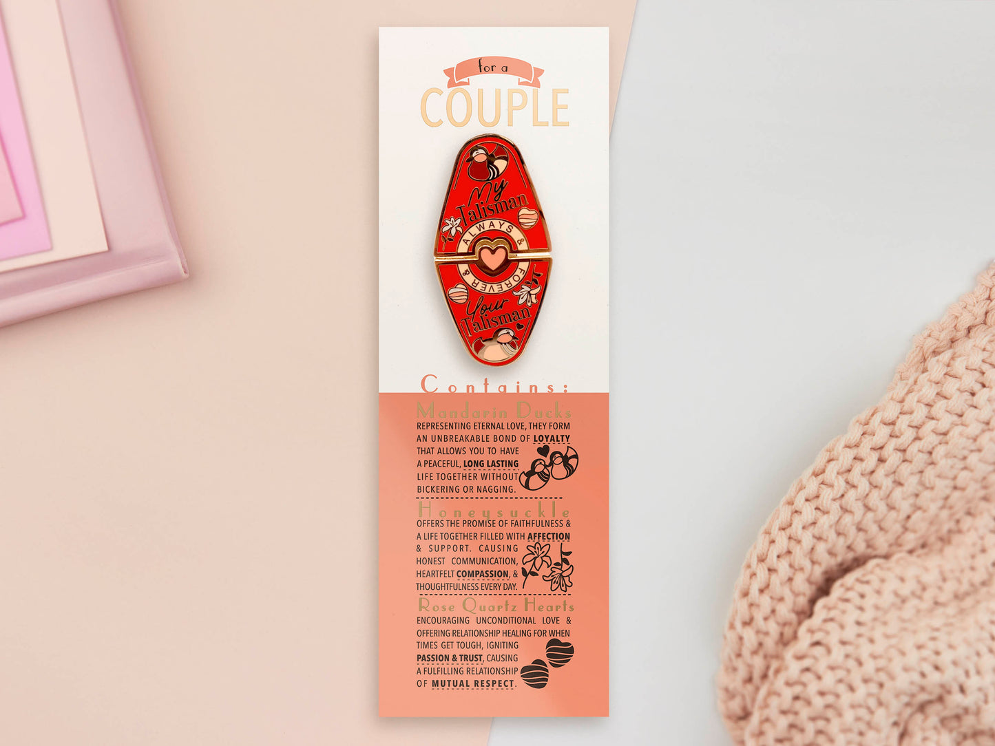 Gold Enamel Talisman Pin with red design and the words couple's Talisman sits on a long white and red backing card with gold accents. The backing card has details the symbolism of the different design elements of the Talisman pin.
