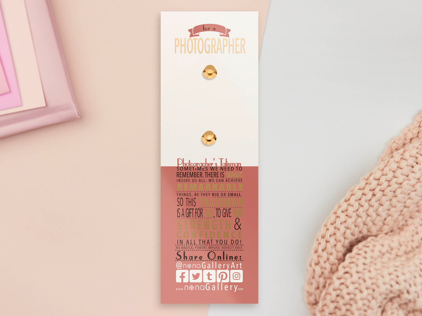 The back of the long white and red backing card with gold accents. The backing card details the symbolism of the different design elements of the Photographer's Talisman pin. Also shown is the two gold locking pin backs attached to the card.
