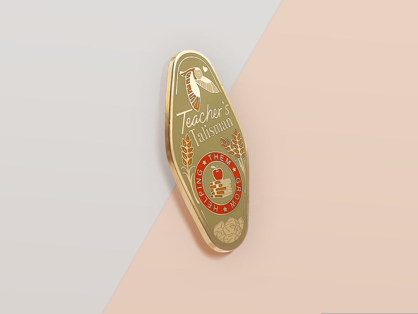 Gold Enamel Talisman Pin with green design and the words Teacher's Talisman, Helping Them Grow. The pins design includes a stack of books and an apple, a barn owl, as well as plants, flowers and crystals.