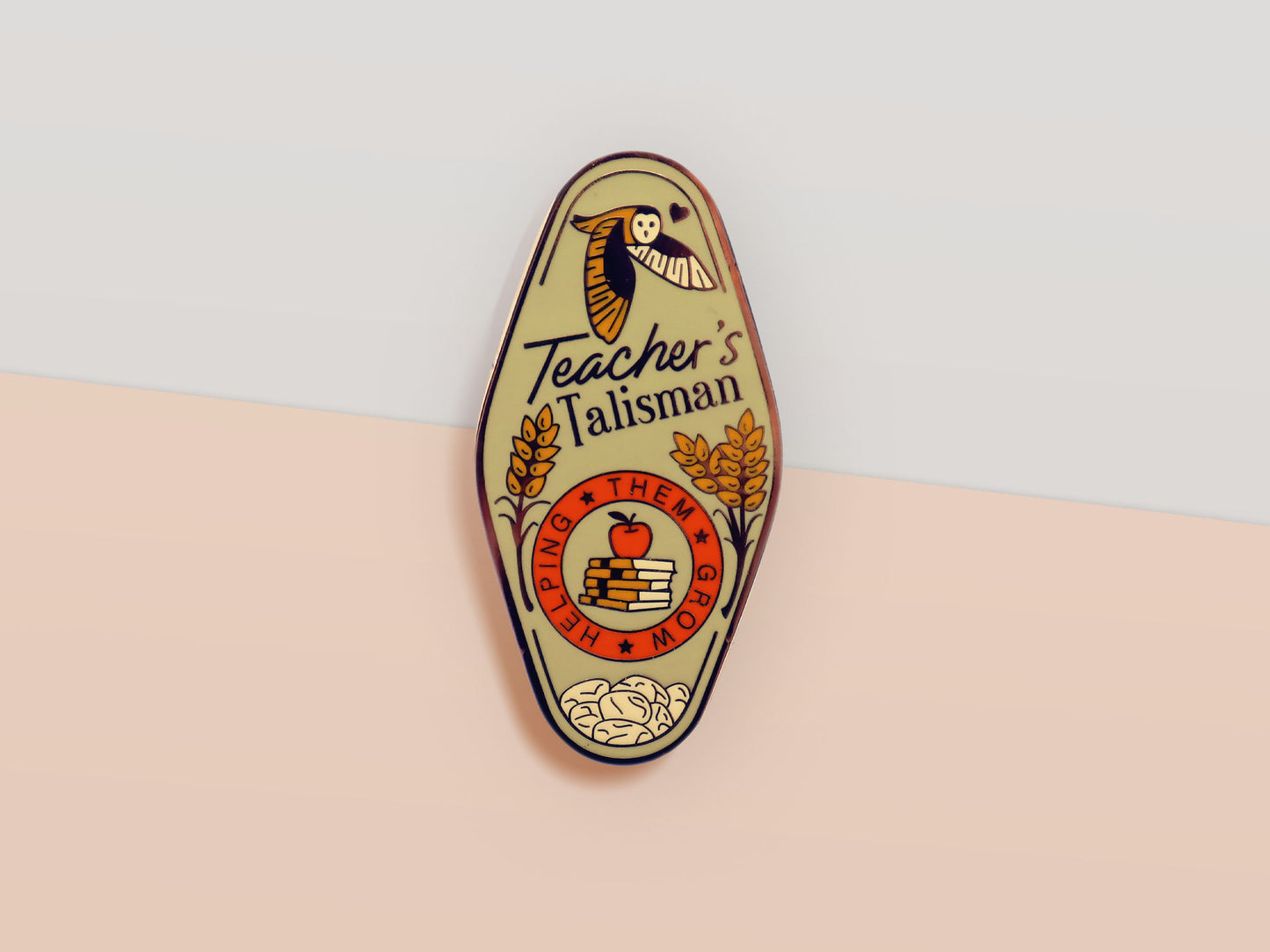 Gold Enamel Talisman Pin with green design and the words Teacher's Talisman, Helping Them Grow. The pins design includes a stack of books and an apple, a barn owl, as well as plants, flowers and crystals.