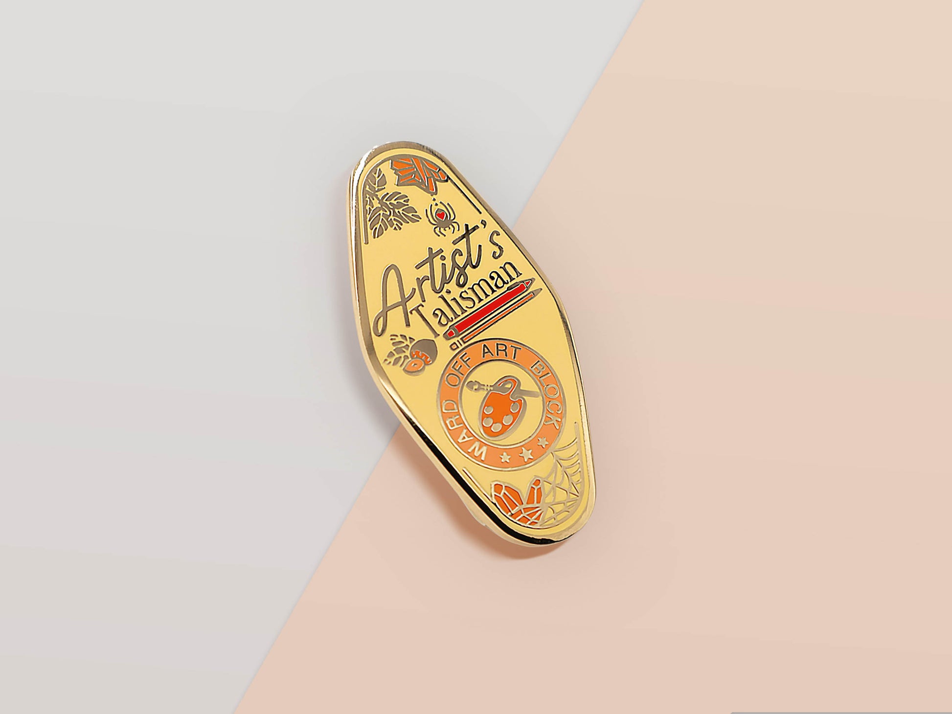 Gold Enamel Talisman Pin with yellow design and the words Artist's Talisman, Ward of Artist's block. The pins design includes a paintbrush, pencil, computer stylus and paint, spider's webs, as well as flowers and crystals.