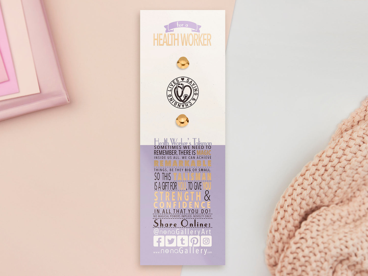 A Health Worker's Talisman gold enamel pin on a gold foiled backing card that outlines the symbolism of the talisman including information and imagery on the Rod of Asclepius, Lavender Stems and Prehnite Crystals