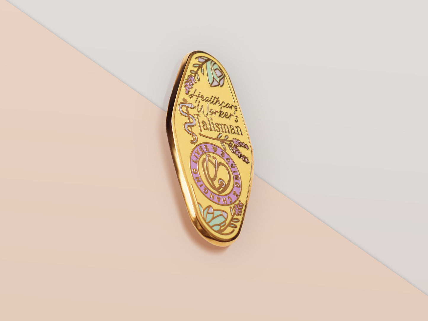 A Health Worker's Talisman gold enamel pin on a gold foiled backing card that outlines the symbolism of the talisman including information and imagery on the Rod of Asclepius, Lavender Stems and Prehnite Crystals